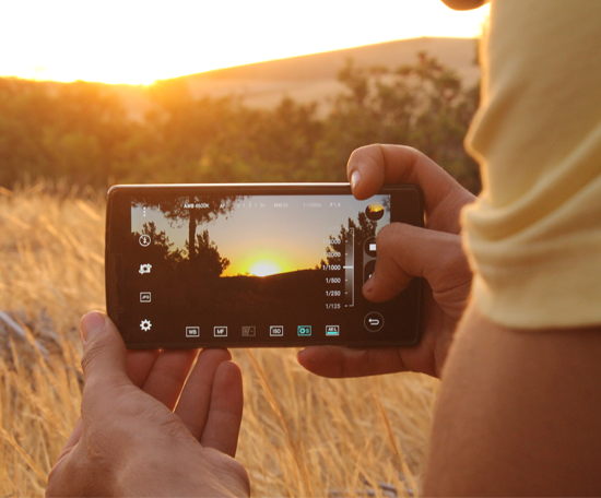 Person holding a smartphone and recording a sunset over a rural landscape.