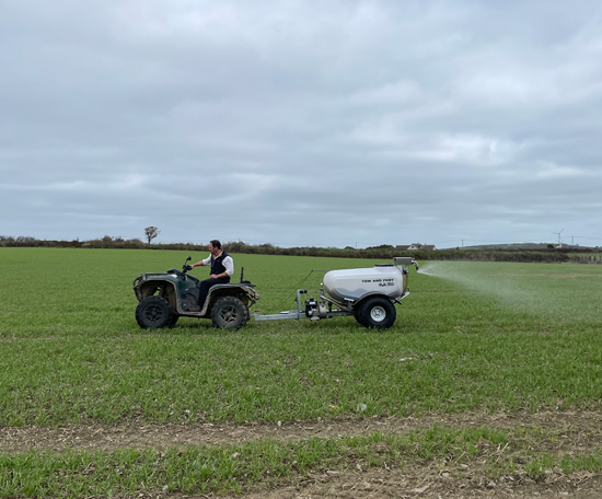 Quad bike towing a sprayer applying liquid fertiliser to a field.