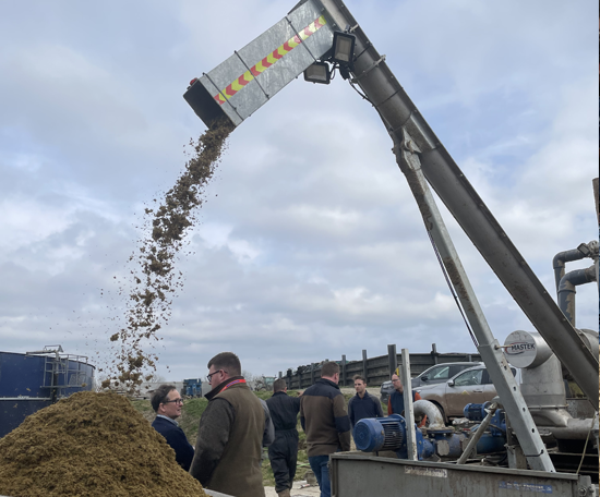 Slurry separator discharging solid material into a pile while a group of people observe during an outdoor farm demonstration.
